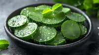 Fresh cucumber slices with water drops and mint leaves in black ceramic bowl on dark background, macro food photography for healthy eating concept.