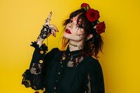 Young Asian woman in gothic style black dress with red roses in hair against yellow background, dramatic makeup and romantic dark fashion aesthetic.