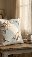 Embroidered floral cushion with pink roses on linen fabric placed on rustic wooden bench near window with soft natural light for cozy home decor styling.