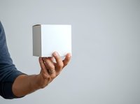 Hand holding white product box with gray side panel against neutral background, suitable for packaging mockups, retail displays, and commercial advertising.