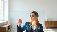 Professional businesswoman in blue suit touching futuristic holographic interface with glowing digital elements in modern office environment.