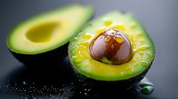Fresh ripe avocado cut in half with pit and olive oil drops on dark background, macro shot showing texture and natural patterns of green flesh.