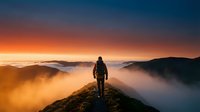 Hiker standing on mountain peak at sunrise above clouds, wearing backpack and looking at golden sky landscape.