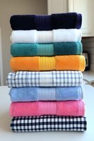 Colorful stack of folded towels and kitchen linens in navy, white, teal, orange, gingham patterns arranged neatly for home organization and laundry concepts.