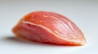 Fresh raw chicken breast fillet with smooth texture and pink color on white background, macro close-up view showing meat fibers and natural patterns.