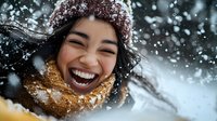Young Asian woman laughing joyfully in winter snow, wearing knit beanie and yellow scarf, with snowflakes falling around her face showing genuine happiness.
