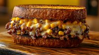 Grilled sandwich with melted cheese, ground beef and corn filling between toasted dark bread slices, served on wooden cutting board. Close up food photography.