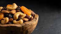 Mixed nuts and dried fruits in wooden bowl on dark background for healthy snacking and cooking ingredients.