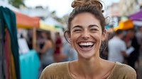 Young Hispanic woman with authentic joyful laughter and bright smile at outdoor market, wearing casual beige sweater, natural makeup and messy bun hairstyle.