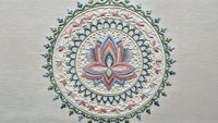 Intricate mandala with lotus flower center featuring ornate geometric patterns and decorative borders in soft pastel colors on textured background.