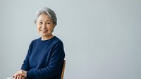 Senior woman with gray hair wearing navy blue sweater, smiling at camera against white background. Portrait for healthcare, wellness, lifestyle, and senior living content.