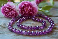 Purple amethyst beaded necklace with pink garden roses on rustic wooden background, romantic jewelry composition for wellness and spiritual healing.