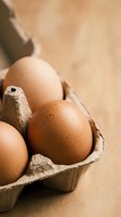 Fresh brown eggs in cardboard carton on rustic wooden surface for cooking and baking ingredients in kitchen preparation.