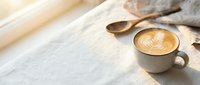 Cozy morning coffee scene with latte art in ceramic cup on wooden table with warm sunlight and soft textile background for cafe lifestyle content.