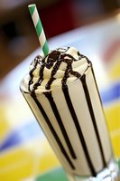 Vanilla milkshake with chocolate syrup drizzle and green striped paper straw in tall glass for dessert menu and beverage advertising.