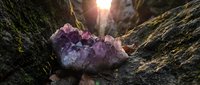 Raw amethyst crystal cluster on rocky surface with dramatic sunlight streaming through canyon walls creating mystical atmosphere for meditation and healing.
