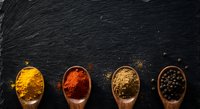 Colorful spices in wooden spoons on dark slate background. Turmeric, paprika, coriander and black pepper arranged in row for culinary cooking and seasoning.