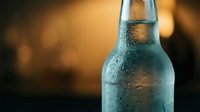 Cold beer bottle with water droplets on warm golden background for refreshing summer drinks and beverage advertising campaigns.