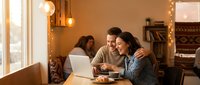 Young couple working together on laptop in cozy cafe with warm lighting and comfortable seating area for remote work and collaboration.