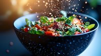 Fresh quinoa salad with cherry tomatoes and herbs in dark bowl with flying seeds creating dynamic cooking motion against blurred kitchen background.
