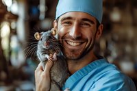 Young male veterinarian in blue scrubs and surgical cap holding gray rat while smiling. Close-up portrait showing positive interaction between medical professional and small pet.