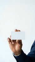 Male professional with dark skin tone holding blank white card against neutral background, wearing dark business suit and silver bracelet, ideal for corporate identity, business card mockups, and professional branding designs.