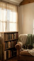 Cozy reading corner with leather armchair, wooden bookshelf, tabby cat and natural light filtering through linen curtains in rustic home interior.