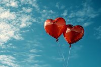 Two red heart-shaped balloons floating against blue sky with white fluffy clouds, symbolizing romance and love. Suitable for Valentine's Day cards and romantic designs.