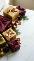 Elegant Christmas gift boxes with gold and burgundy ribbons arranged on marble surface with pine branches, pinecones and dried orange slices for holiday celebrations.