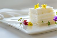 White soap bars stacked on marble tray decorated with colorful edible flowers for natural skincare and spa wellness routine.