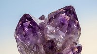 Cluster of raw amethyst crystals with deep purple hues and natural facets, photographed against a soft gradient background.