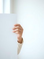 Female hand holding blank white card or paper behind wall, studio shot with minimalist aesthetic for advertising and marketing campaigns.