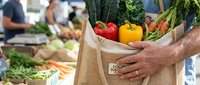 Farmer holding paper bag filled with fresh red and yellow bell peppers at farmers market, sustainable shopping and local produce selection.