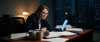 Professional businesswoman working late at office desk with laptop and documents in modern corporate environment at night.