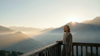 Woman in casual cardigan standing on wooden railing overlooking misty mountain valley at sunrise, contemplative travel and nature scene for lifestyle and wellness content.