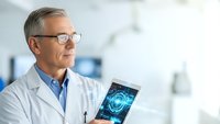 Middle-aged Caucasian male doctor in white coat examining brain scan on tablet in modern medical facility for healthcare technology and diagnosis.