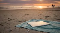 Abandoned blue fabric lies on sandy beach at golden hour sunset with distant figures and ocean waves in background, suitable for loss, forgotten, abandonment, or environmental themes.