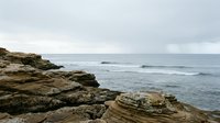 Rocky coastal landscape with layered stone formations and ocean waves under overcast sky, suitable for travel, nature, and environmental design projects.