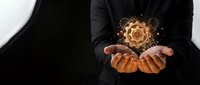 Professional businessman in dark suit holding glowing golden gear mechanism above cupped hands representing innovation, technology solutions and business development.