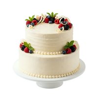 Two-tier cream frosted cake with fresh berries, pearl piping details, and mint leaves on white cake stand for celebrations.