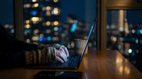 Professional working late at night on laptop with city lights bokeh background for business and technology concepts.