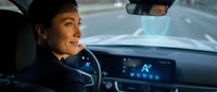 Young male driver with olive complexion operating vehicle with advanced digital dashboard display and holographic interface technology.