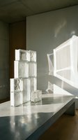 Stacked translucent glass blocks with varied textures casting geometric shadows on concrete surface and sage wall, modern architectural design element for interior styling and contemporary decor projects.