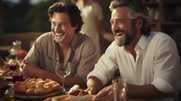 Two mature Caucasian men laughing heartily at dinner party, sharing bread and wine in warm evening light, creating authentic friendship moment at rustic wooden table.