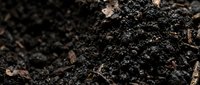 Rich dark soil texture with organic matter and decomposed leaves creating fertile ground for gardening and agriculture applications.