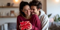 Happy young couple embracing while holding red gift box in cozy home interior during holiday celebration or special occasion.