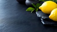 Fresh yellow lemons with green leaves on black slate board against dark background, copy space for text. Minimalist food photography composition.