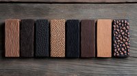 Artisanal chocolate bars with textured surfaces arranged in row on rustic wooden background, showcasing variety of patterns and designs in dark and milk chocolate.