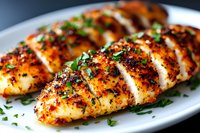 Grilled chicken breasts seasoned with herbs and spices, sliced and garnished with fresh chopped parsley on white plate, close up view of juicy poultry dish.