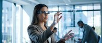 Professional businesswoman using augmented reality smart glasses in modern office, interacting with virtual interface technology for future work.